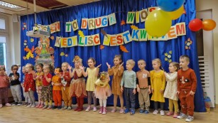 dzieci stoją w kolorowych strojach na tle dekoracji jesiennej