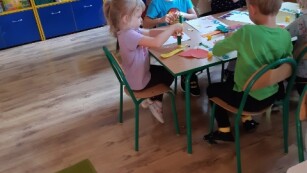 dzieci siedzą przy stole i robią pracę plastyczną