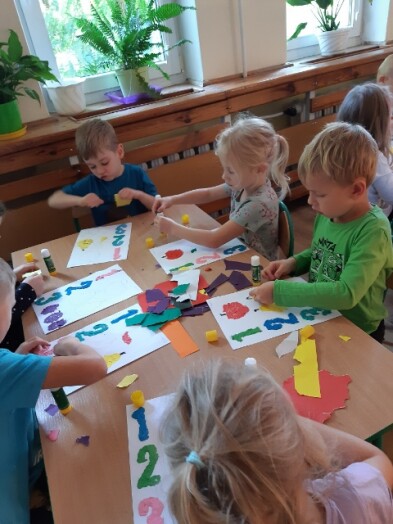 dzieci wyklejają na kartce cyfry i figury z kolorowego papieru
