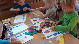 dzieci wyklejają na kartce cyfry i figury z kolorowego papieru