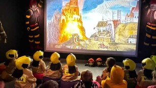 Dzieci w strojach strażaków oglądają film o płonących budynkach