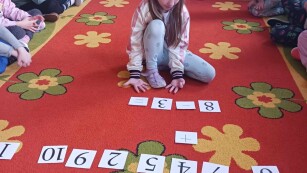 Dziewczynka na dywanie układa działanie z liczbami