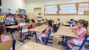 Dzieci siedzą w szkolnych ławkach oglądają występ starszych kolegów
